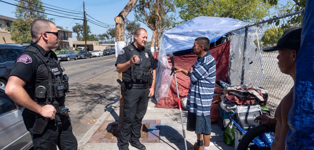 California patrol officers engaging with an unhoused individual during a field contact, handheld biometric device in use