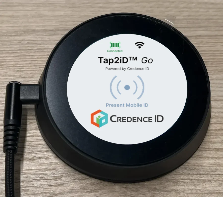Tap2iD Go mDL reader on a counter, round color display lit, USB-C cable attached